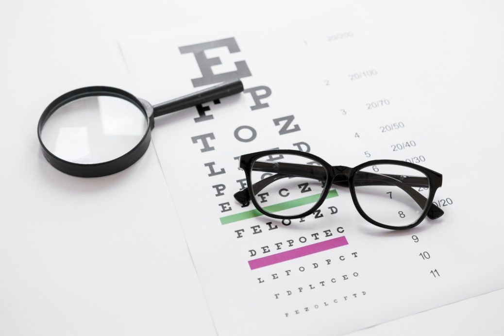 óculos e lupa em cima de tabela usada no teste de acuidade visual