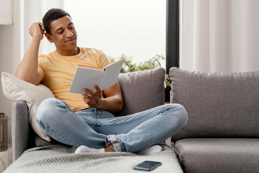 Jovem sentado no sofá lendo livro